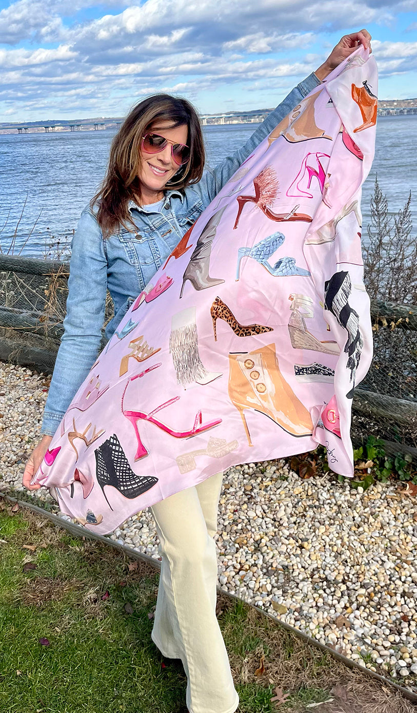 Image of a beautiful woman outside by ocean  and holding up the Designer Shoe Print Scarf diagonally across her body to show off print.